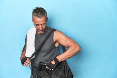 Mavi stüdyo arka planında spor çantalı bir sporcu.