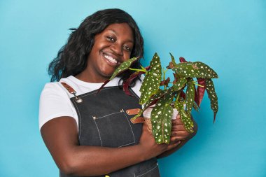 Kibar kıvrımlı bahçıvan mavi arka planda sevgiyle bir bitki tutuyor.