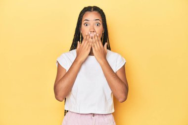 Sarı stüdyo arkaplanındaki genç Endonezyalı kadın şok geçirdi. Ağzını ellerle kapladı. Yeni bir şey keşfetmek için sabırsızlanıyor..