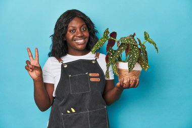 Stüdyoda iki numarayı parmaklarıyla gösteren kıvrımlı bir bahçıvan..