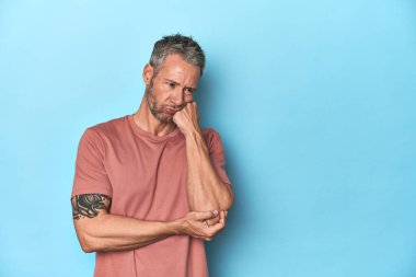 Mavi arka planda oturan orta yaşlı, beyaz bir adam üzgün ve dalgın bir şekilde fotokopi odasına bakıyor..