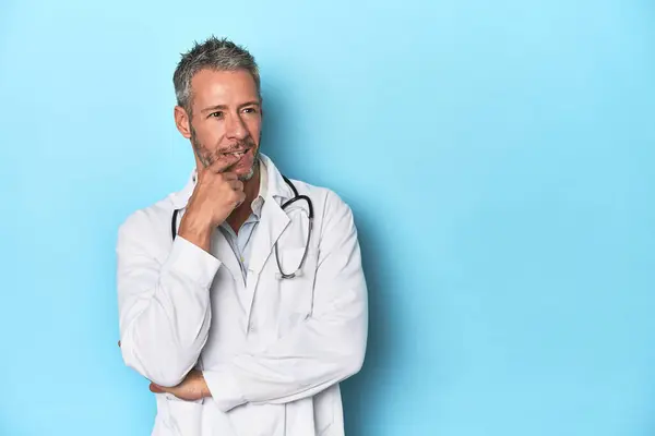 Caucasian Middle Aged Doctor Blue Background Relaxed Thinking Something Looking — Stock Photo, Image