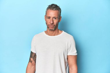 Orta yaşlı bir adam mavi stüdyo arka planında poz veriyor.