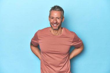 Mavi arka plandaki orta yaşlı beyaz adam mutlu, güler yüzlü ve neşeli..