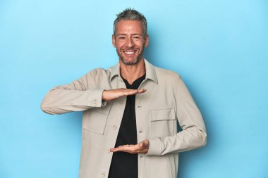 Mavi arka planda orta yaşlı beyaz bir adam iki eliyle bir şey tutuyor, ürün sunumu..