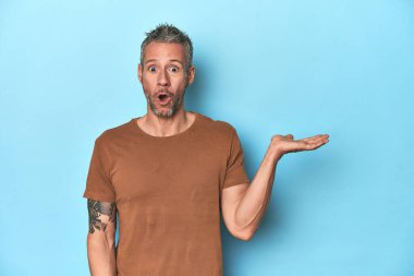 Mavi arka planda oturan orta yaşlı beyaz adam, avuç içi fotokopi alanını elinde tutmaktan çok etkilendi..