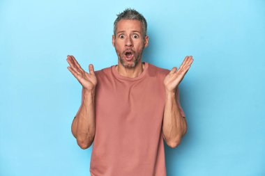 Mavi arka plandaki orta yaşlı beyaz adam şaşırdı ve şok oldu..