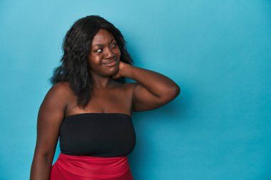 Genç Afro-Amerikan kıvrımlı kadın başının arkasına dokunuyor, düşünüyor ve bir seçim yapıyor..