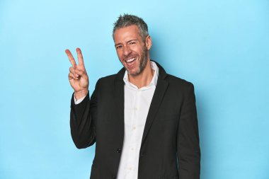 Beyaz iş adamı, mavi arka planda orta yaşlı neşeli ve kaygısız parmakları olan bir barış sembolü gösteriyor..