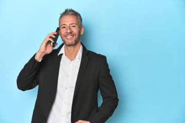 Takım elbiseli bir işadamı telefonda konuşuyor, mavi stüdyo arkaplanı.
