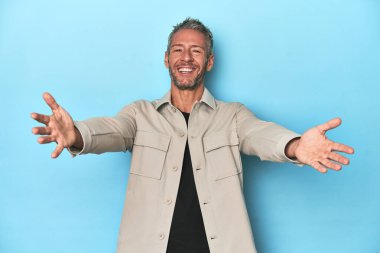 Mavi arka plandaki orta yaşlı beyaz adam kameraya sarıldığı için kendinden emin..