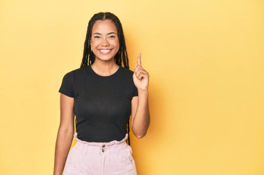 Sarı stüdyo arkaplanındaki Endonezyalı genç kadın parmaklarıyla bir numarayı gösteriyor..