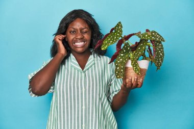 Stüdyoda bitki tutan kıvrımlı bahçıvan elleriyle kulaklarını kapatıyor..