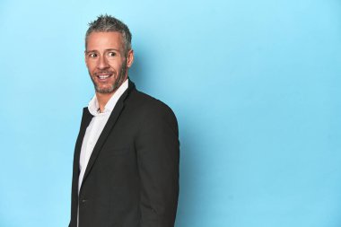 Beyaz iş adamı, orta yaşlı, mavi arka planda. Gülümsüyor, neşeli ve keyifli..