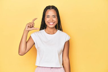 Sarı stüdyo stüdyosundaki Endonezyalı genç kadın elinde işaret parmaklarıyla küçük bir şey tutuyor, gülümsüyor ve kendinden emin..