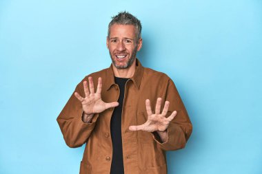 Mavi arka planda orta yaşlı beyaz bir adam tiksinti belirtisi gösteren birini reddediyor..