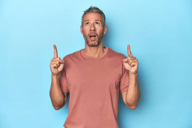 Orta yaşlı, beyaz, mavi arka planda ağzı açık, üst tarafı gösteren bir adam..