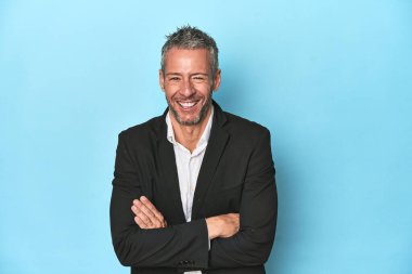 Beyaz iş adamı, orta yaşlı, mavi arka planda gülüyor ve eğleniyor..
