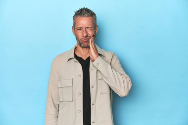 Mavi arka plandaki orta yaşlı beyaz adam güçlü bir diş ağrısı, azıdişi ağrısı var..