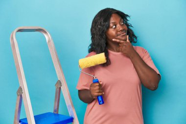 Boya silindiri ve merdiveni olan kıvrımlı bir kadın şüpheli ve şüpheci bir ifadeyle yana bakıyor..