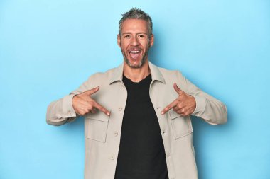 Mavi zemin üzerinde orta yaşlı beyaz bir adam parmağını göstererek şaşırdı ve gülümsedi..