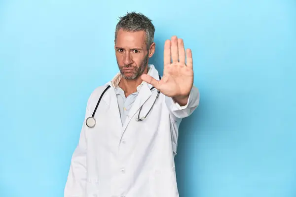 Biały Lekarz Średnim Wieku Niebieskim Tle Wyciągniętą Ręką Znakiem Stopu — Zdjęcie stockowe