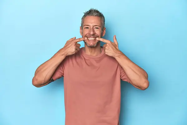 Orta Yaşlı Beyaz Adam Mavi Arka Planda Gülümsüyor Parmaklarını Ağıza — Stok fotoğraf