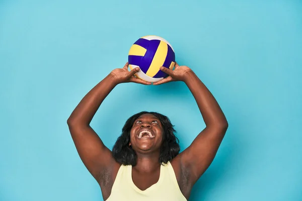 在蓝色背景下练习排球的体形纤细的卷曲女子 — 图库照片