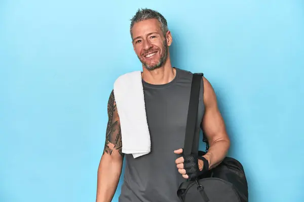 Athlete with gym backpack on blue background happy, smiling and cheerful.