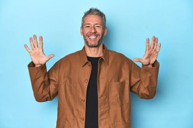 Mavi arka planda orta yaşlı beyaz bir adam 10 numarayı elleriyle gösteriyor..