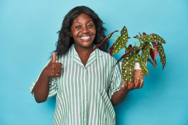 Stüdyoda çiçek tutan kıvrımlı bahçıvan gülümsüyor ve başparmağını kaldırıyor.