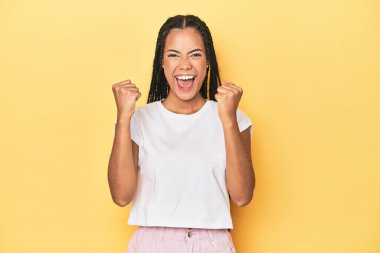 Sarı stüdyo arkaplanındaki Endonezyalı genç kadın gamsız ve heyecanlı tezahüratlar yapıyor. Zafer konsepti.