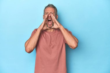 Orta yaşlı beyaz adam mavi arka planda heyecanlı bir şekilde bağırıyor..