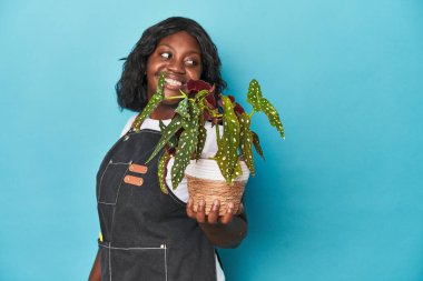 Stüdyoda çiçek tutan kıvrımlı bahçıvan gülümseyen, neşeli ve hoş bir tarafa bakıyor..