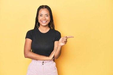 Sarı stüdyo arkaplanındaki Endonezyalı genç kadın mutlu bir şekilde işaret parmağıyla işaret ederek gülümsedi..