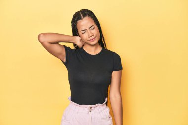 Sarı stüdyodaki genç Endonezyalı kadın sabit yaşam tarzından dolayı boyun ağrısı çekiyor..