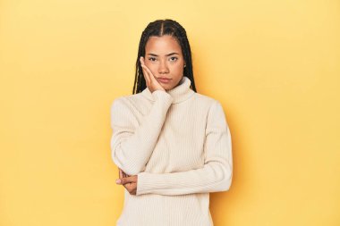 Sarı stüdyo arkaplanındaki genç Endonezyalı kadın sıkılmış, yorgun ve dinlenmeye ihtiyacı var..