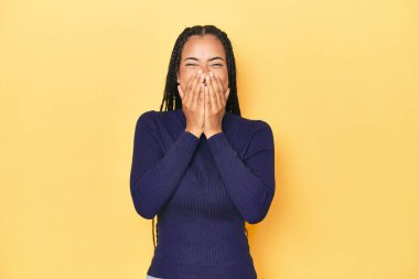 Sarı stüdyo stüdyosundaki genç Endonezyalı kadın bir şeye gülüyor, elleriyle ağzını kapatıyor..