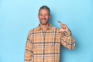 Orta yaşlı beyaz bir adam mavi arka planda. Elinde küçük bir şey tutuyor, gülümsüyor ve kendinden emin..