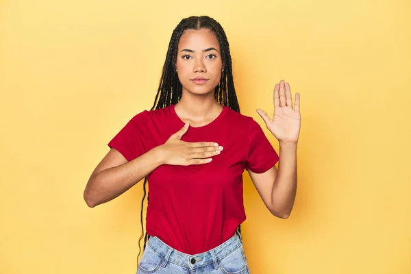 黄色いスタジオのバックドロップの若いインドネシアの女性は誓いを立て 胸に手を置く — ストック写真