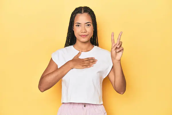 Young Indonesian woman on yellow studio backdrop taking an oath, putting hand on chest.