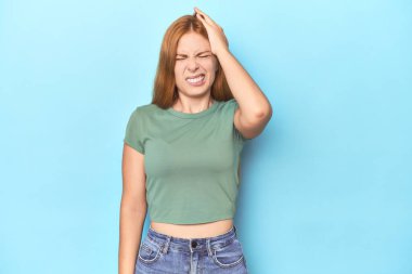 Mavi arka plandaki kızıl saçlı genç kadın bir şeyi unutuyor. Alnına avuç içi ve kapalı gözlerle vuruyor..