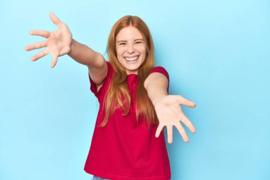 Mavi arka plandaki kızıl saçlı genç kadın kameraya sarıldığı için kendinden emin..