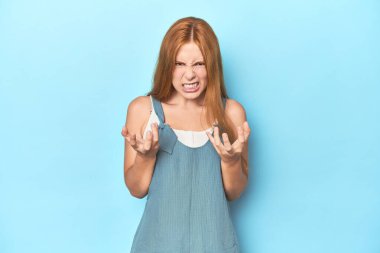 Mavi arka plandaki kızıl saçlı genç kadın gergin elleriyle çığlık atıyor..