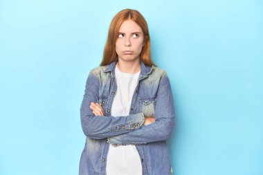 Mavi arka plandaki kızıl saçlı genç kadın tekrarlanan bir görevden bıktı..