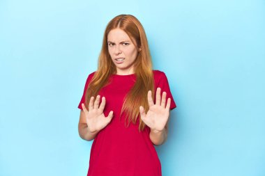 Mavi arka plandaki kızıl saçlı genç kadın tiksinti gösteren birini reddediyor..