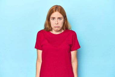 Mavi arka plandaki kızıl saçlı genç kadın omuzlarını silker ve gözleri açık kalır..