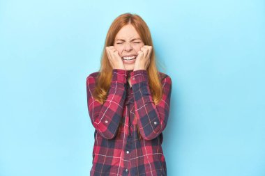 Mavi arka planda ağlayan kızıl saçlı genç bir kadın. Acı ve kafa karışıklığı gibi bir şeyden mutsuz..