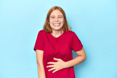 Mavi arka plandaki kızıl saçlı genç kadın karnına dokunuyor, nazikçe gülümsüyor, yemek yiyor ve tatmin oluyor..