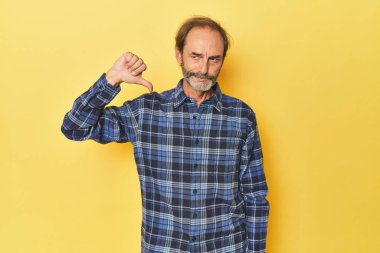 Sarı stüdyoda orta yaşlı bir adam baş parmağını aşağı gösteriyor, hayal kırıklığı konsepti..